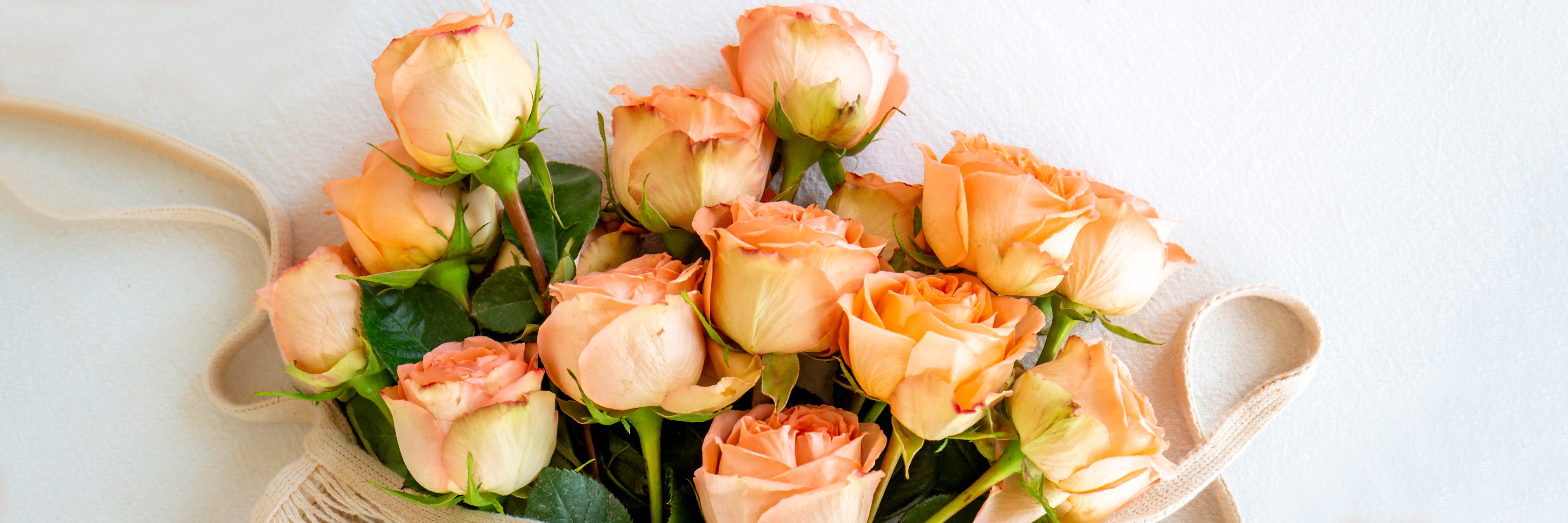 Freshly picked peach roses with green leaves, elegantly arranged in a soft, natural setting.