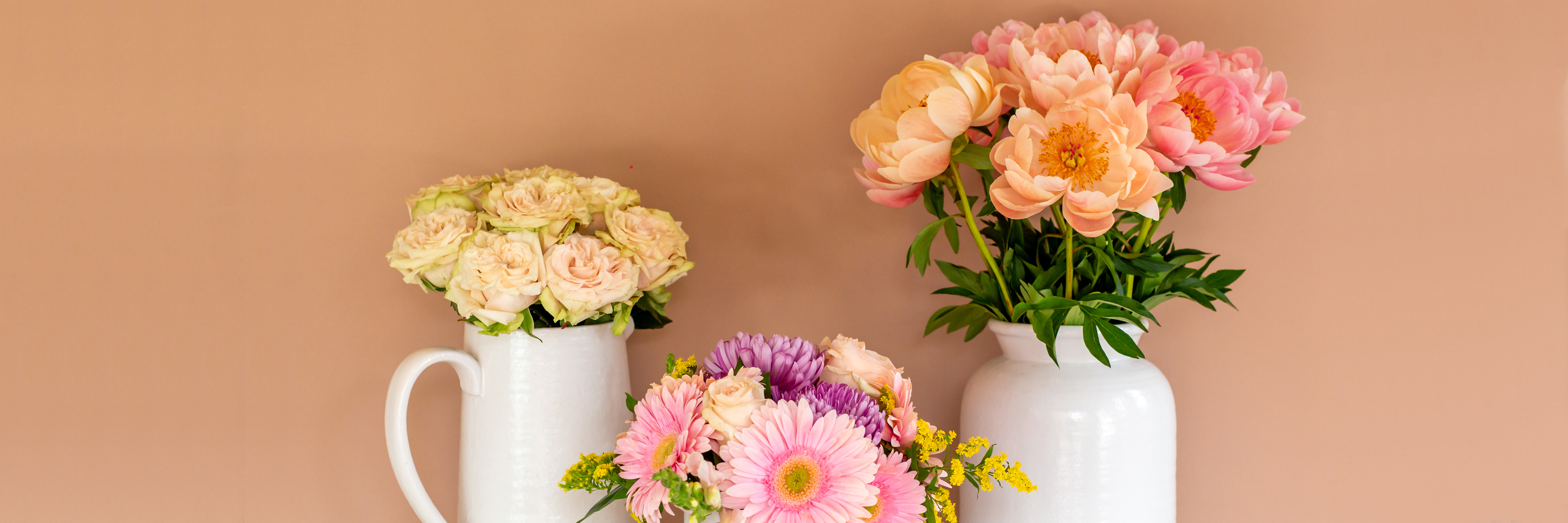 Elegant floral display featuring soft pink peonies and vibrant gerbera daisies in white vases.