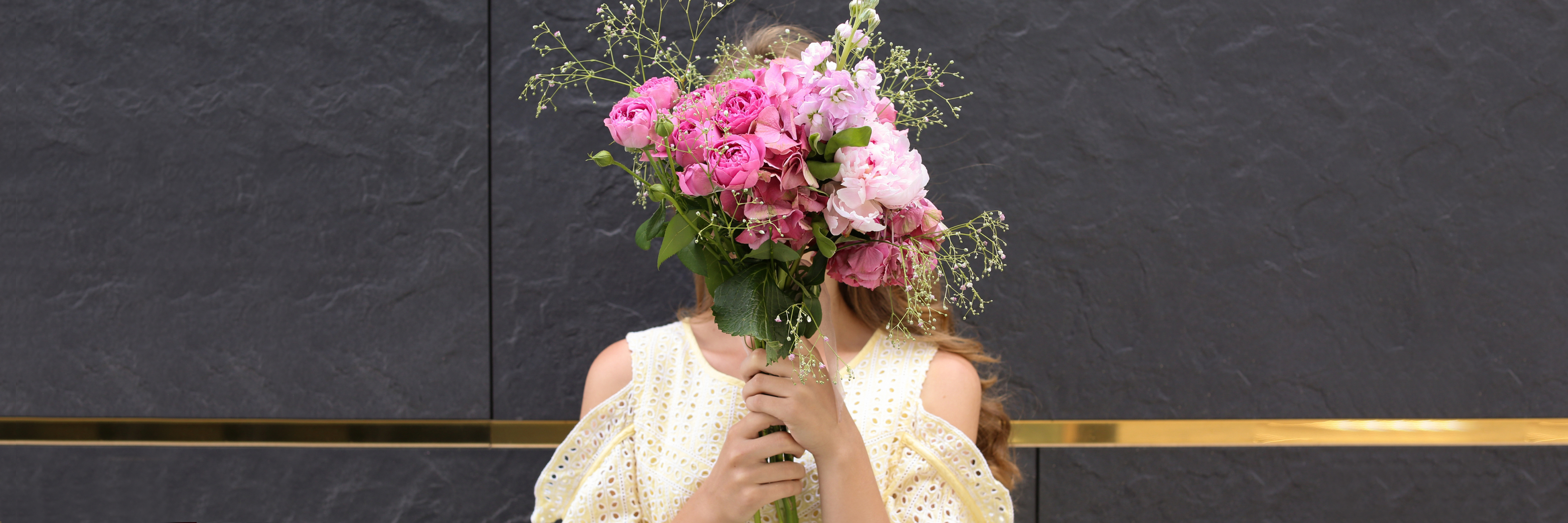 A woman hides her face behind a vibrant bouquet of pink flowers, showcasing nature’s beauty.