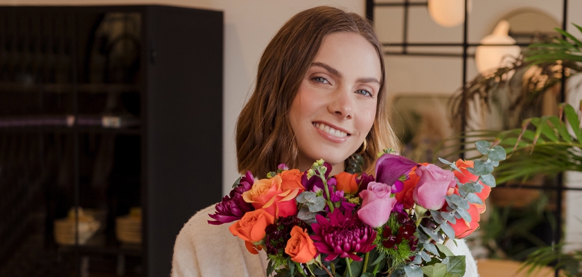 A smiling woman holds a vibrant bouquet of multicolored flowers, showcasing cheerful spring blooms.