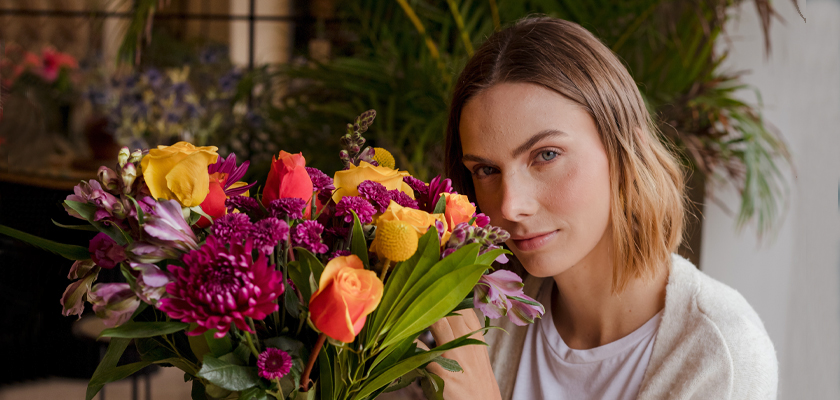 A woman holding a vibrant bouquet of mixed flowers, showcasing bright colors and textures.