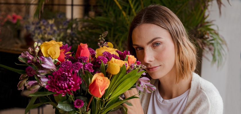 A woman holding a vibrant bouquet of mixed flowers, showcasing bright colors and textures.