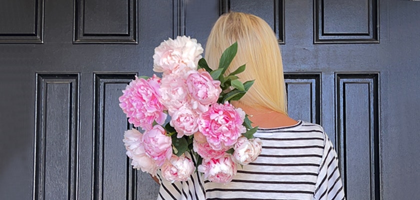 A woman in a striped shirt holding a beautiful bouquet of pink peonies against a dark door.