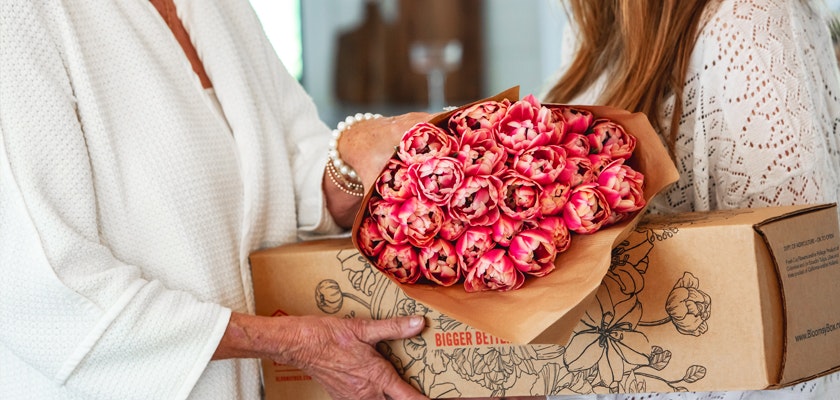 Two women exchanging a beautiful bouquet of pink tulips in a stylish floral arrangement.