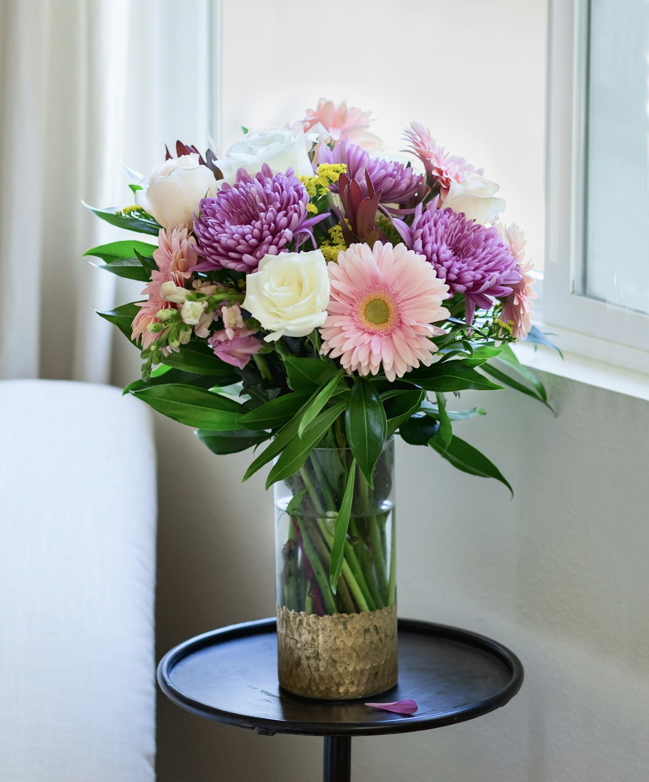 A vibrant floral arrangement featuring pink gerbera daisies, purple chrysanthemums, and white roses.
