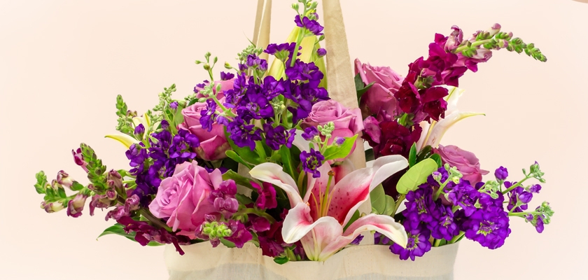 Vibrant floral arrangement featuring pink roses, purple blooms, and white lilies in a chic tote.