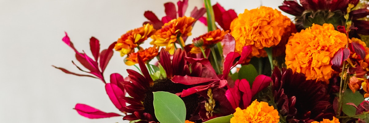 Vibrant floral arrangement featuring marigolds, zinnias, and rich foliage in warm autumn hues.
