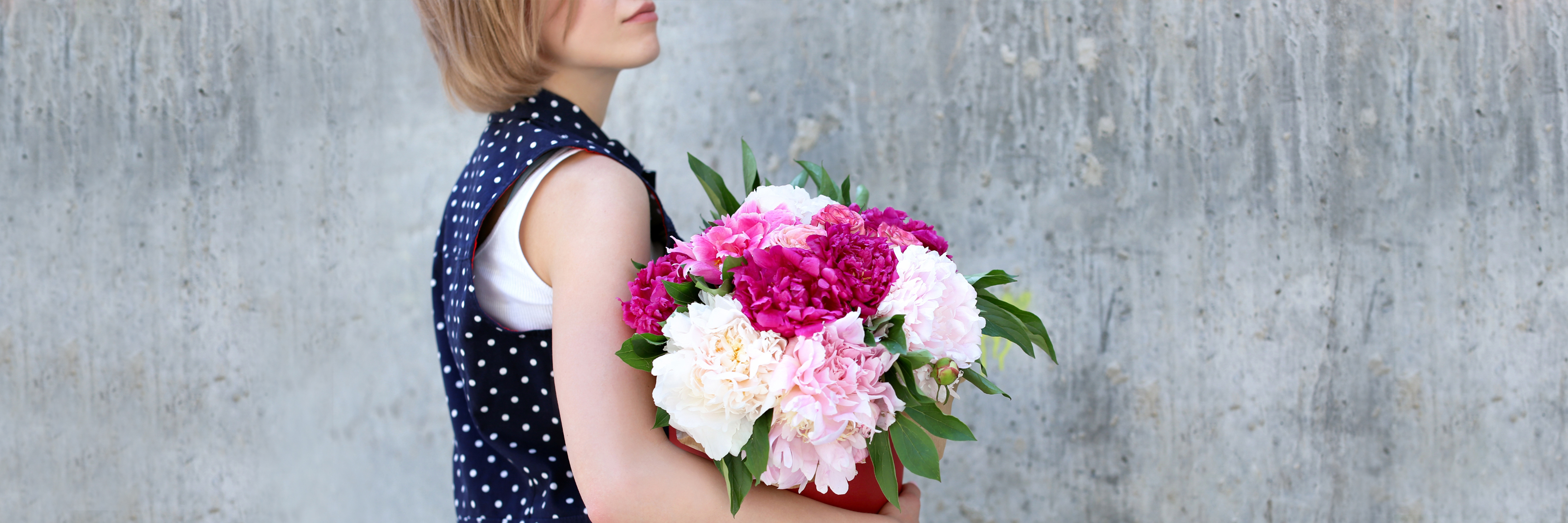 A young woman in a polka dot dress holding a vibrant bouquet of peonies and pink flowers.