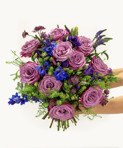 Lavender rose bouquet with vibrant blue delphiniums and lush greenery, elegantly arranged.