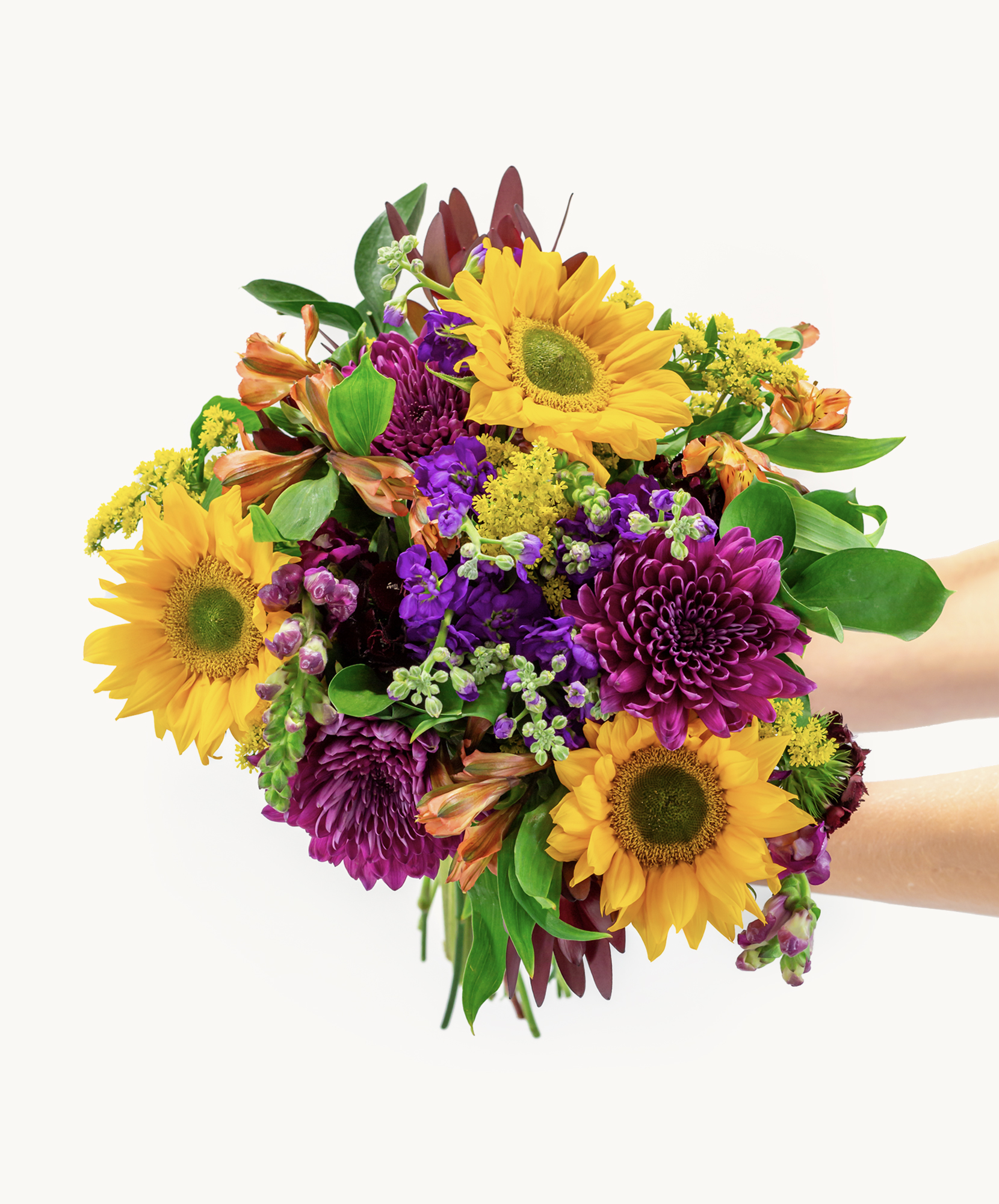 Vibrant bouquet featuring sunflowers, purple blooms, and lush greenery in a hand-held arrangement.
