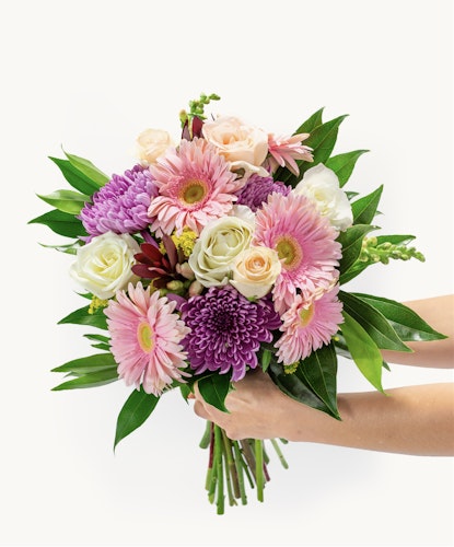 Vibrant floral bouquet featuring pink gerbera daisies, roses, and lush greenery.