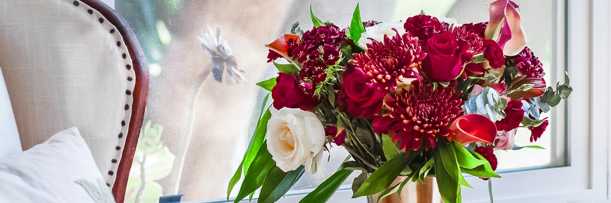 Vibrant floral arrangement featuring red roses, white blooms, and greenery by a sunlit window.