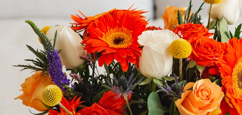 Vibrant floral arrangement featuring orange gerbera daisies, white roses, and colorful accents.