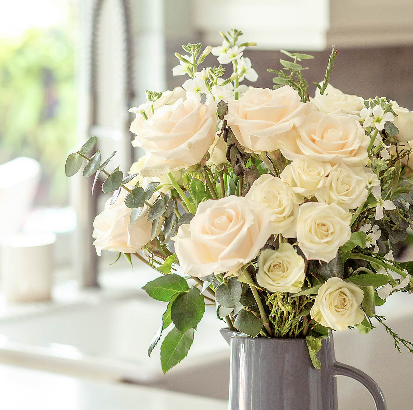 Elegant arrangement of white and soft pink roses with greenery in a charming vase.