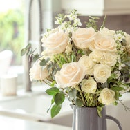 Elegant arrangement of white and soft pink roses with greenery in a charming vase.