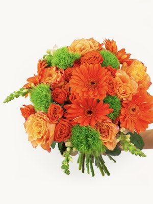 Vibrant bouquet featuring orange gerbera daisies and soft peach roses, accented with lush greenery.