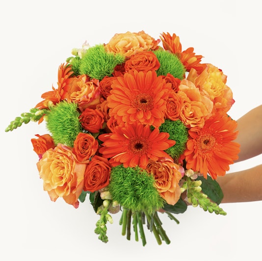 Vibrant bouquet featuring orange gerbera daisies and soft peach roses, accented with lush greenery.
