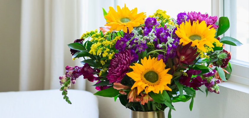 Vibrant bouquet featuring sunflowers, purple blooms, and greenery, brightening up any room.