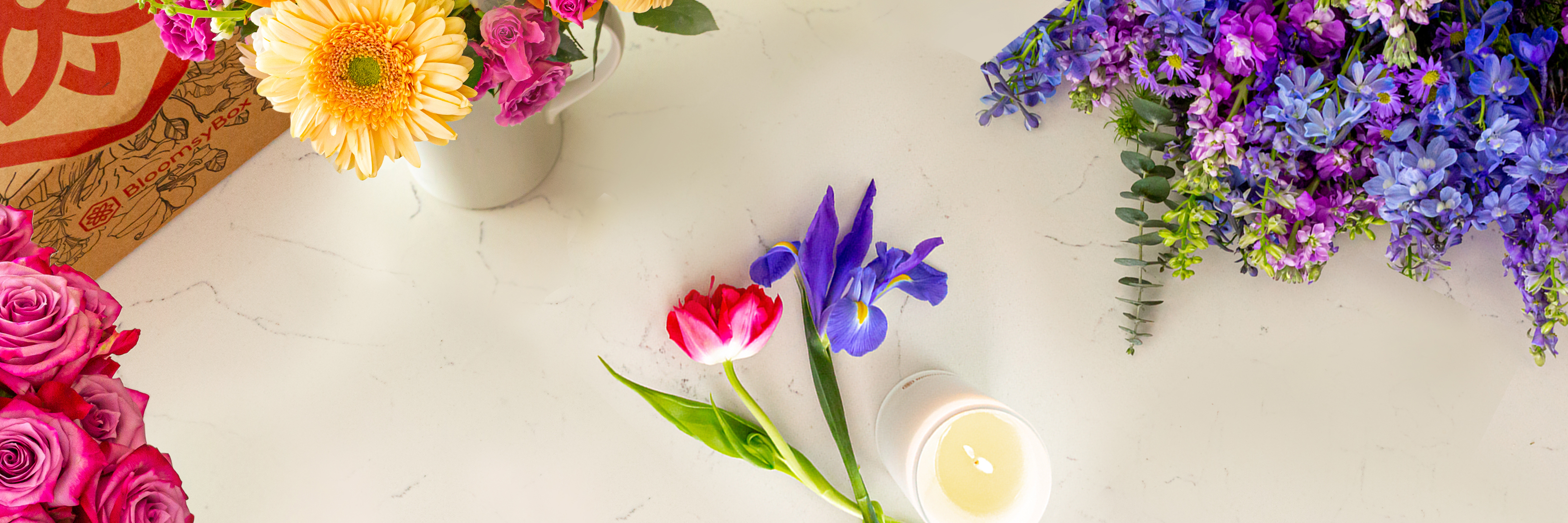 Vibrant floral arrangement featuring tulips, daisies, and irises beside a lit candle.