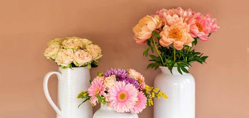 A charming arrangement of pink peonies, creamy roses, and vibrant daisies in elegant vases.