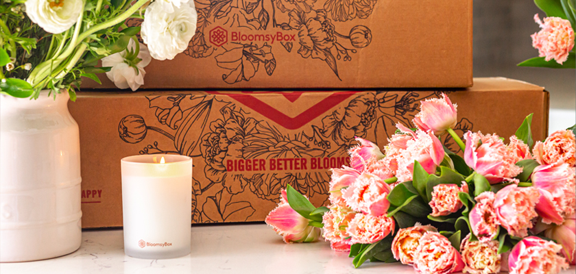 A beautifully arranged floral display with pink tulips, a candle, and a BloomsyBox subscription box.