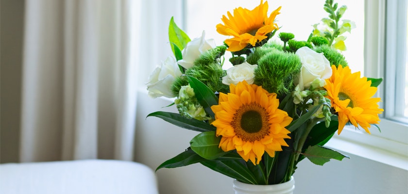 Vibrant bouquet featuring sunflowers, white roses, and lush greenery in a stylish vase.