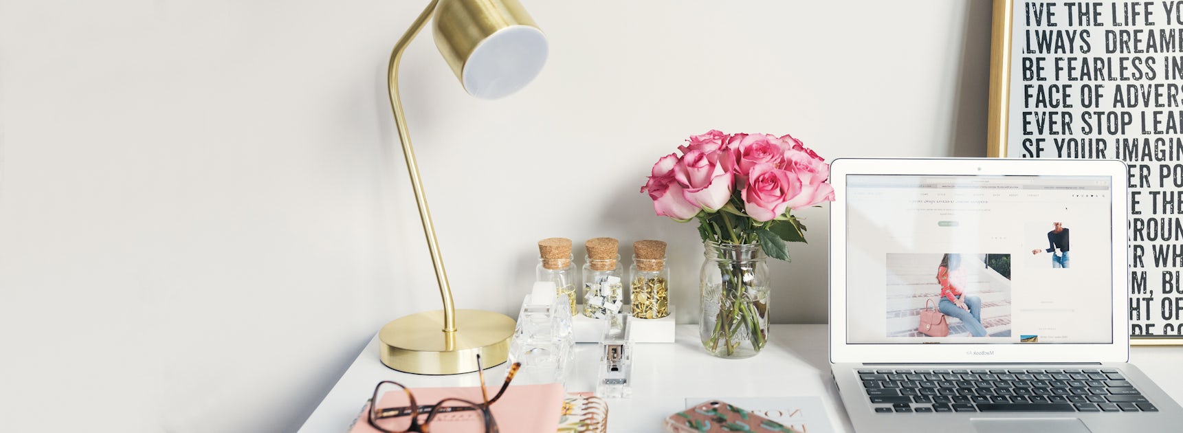 A stylish workspace featuring a laptop, pink rose bouquet, and modern lamp.