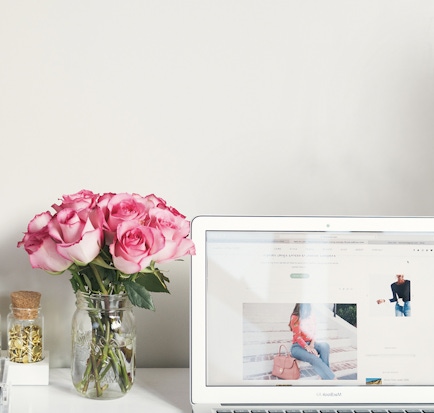 A charming bouquet of pink roses in a glass jar beside a laptop, creating a cozy workspace vibe.