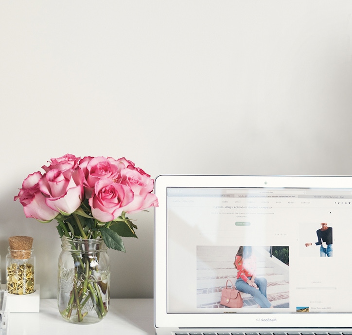 A charming bouquet of pink roses in a glass jar beside a laptop, creating a cozy workspace vibe.
