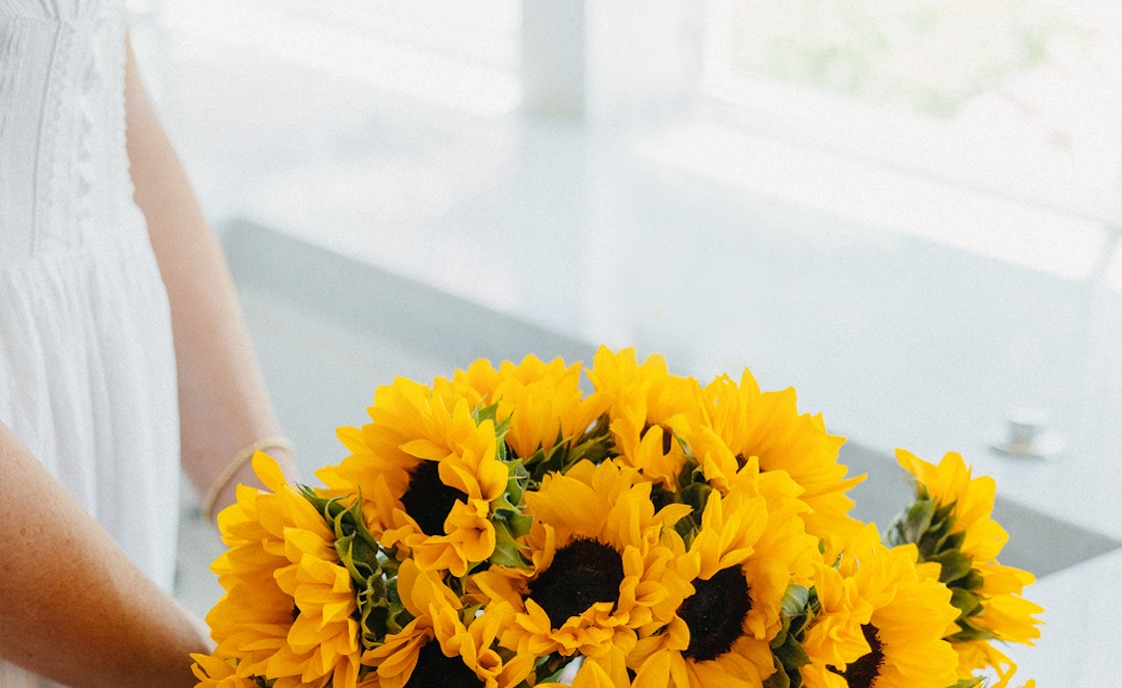 A vibrant bouquet of sunflowers held by a person, showcasing cheerful yellow petals and green stems.