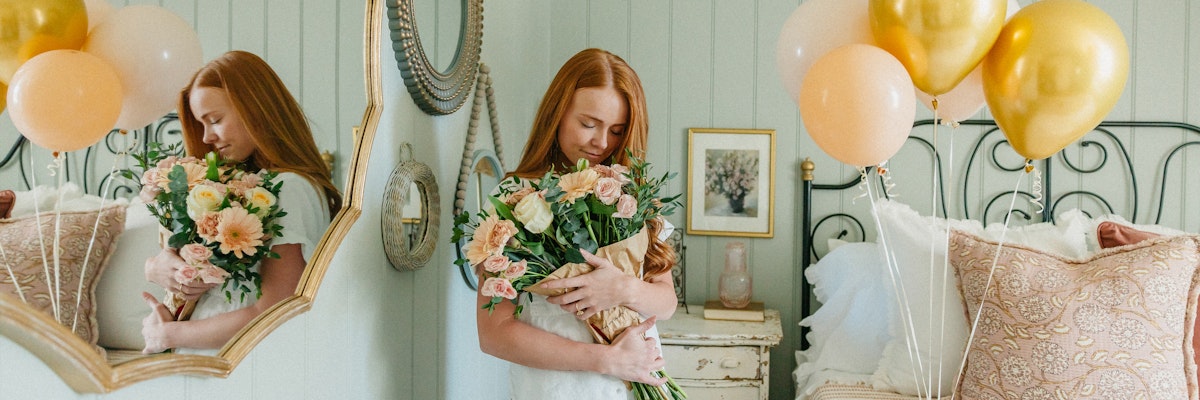 A young girl embraces a beautiful floral bouquet, surrounded by soft balloons in an elegant room.