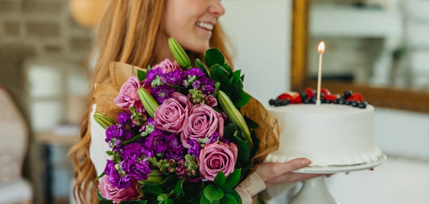A joyful celebration with a vibrant bouquet of purple and pink flowers alongside a birthday cake.