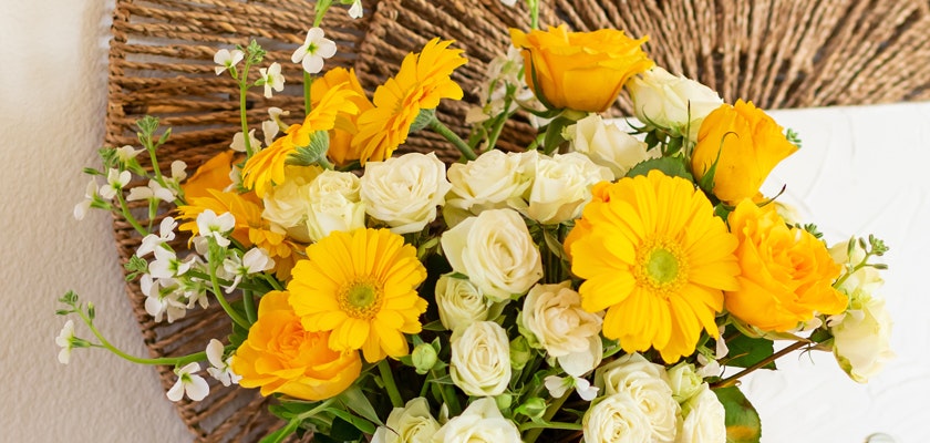 Bright floral arrangement featuring yellow roses, gerbera daisies, and white blooms.