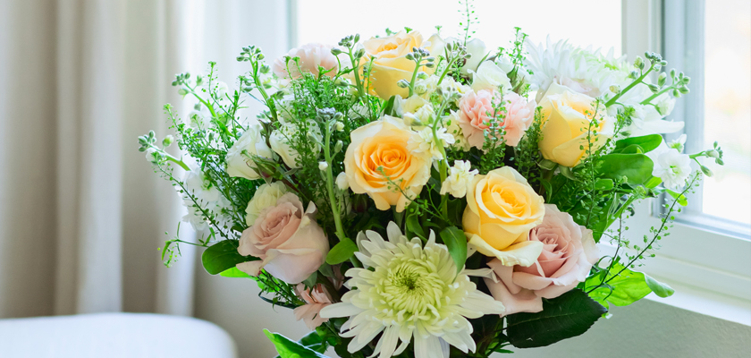 A lovely bouquet featuring yellow and pink roses, white daisies, and lush greenery.