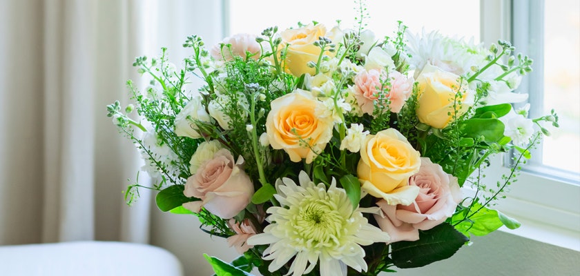 A lovely bouquet featuring yellow and pink roses, white daisies, and lush greenery.