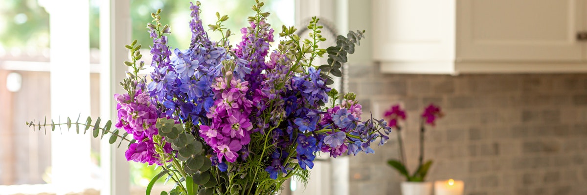 Vibrant bouquet of purple and pink flowers with lush greenery in a stylish kitchen setting.