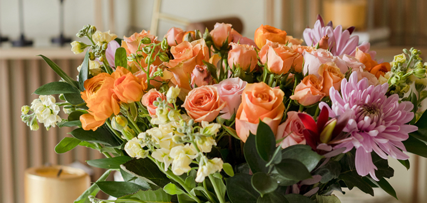 A vibrant bouquet featuring peach roses, colorful blooms, and lush greenery for joyful occasions.
