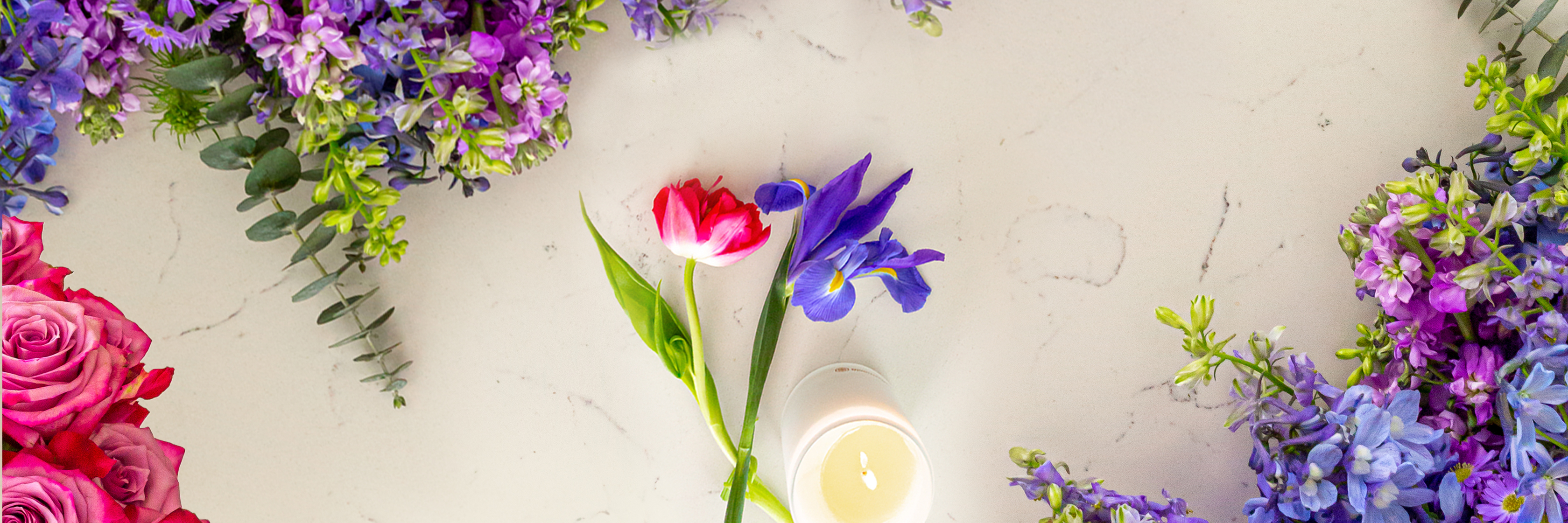 Vibrant floral arrangement featuring pink roses, purple blooms, and a delicate candle centerpiece.