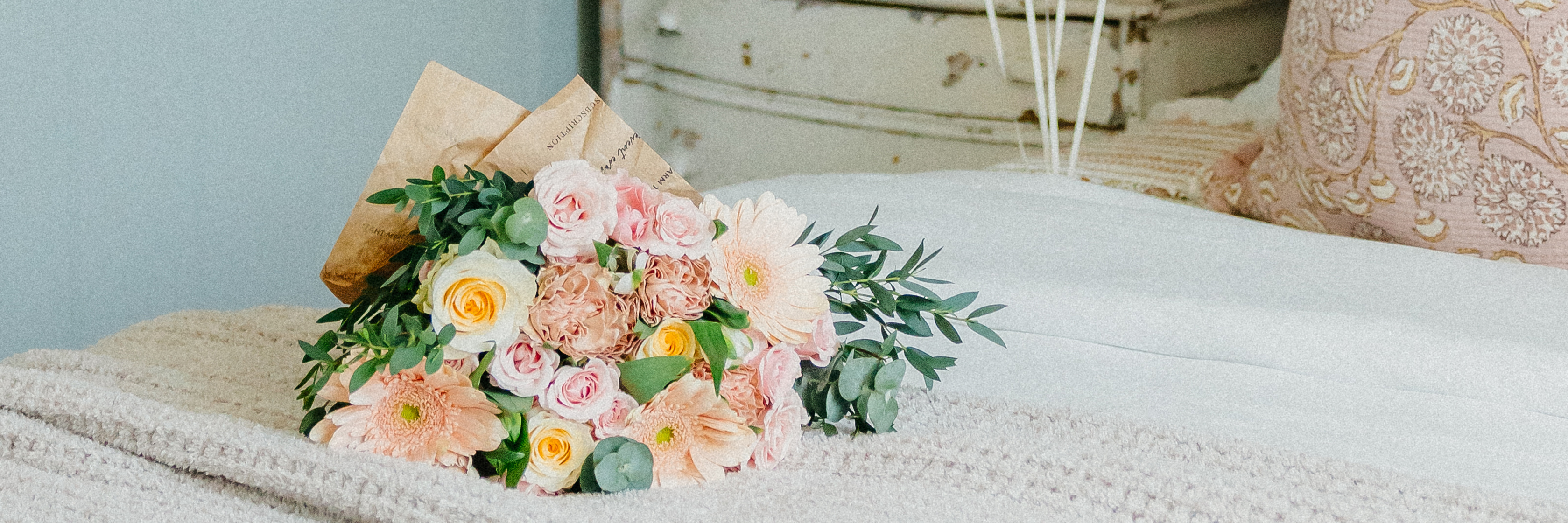 A charming bouquet of pastel flowers with greenery, elegantly arranged on a soft bed covering.