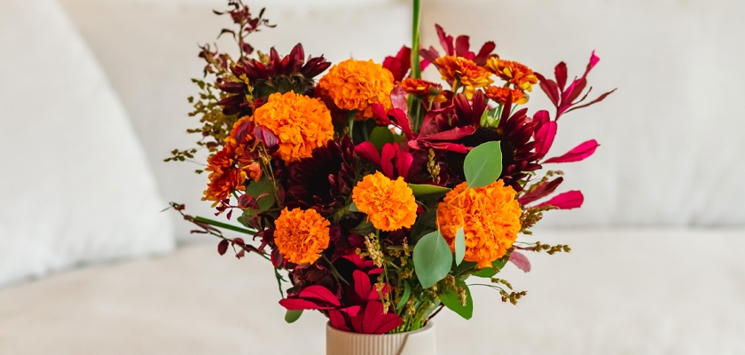 Vibrant bouquet of marigolds and colorful foliage in a chic vase, ideal for decorating spaces.
