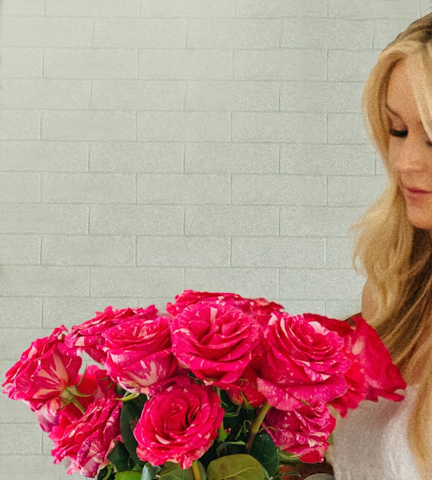 Vibrant pink roses in a stunning bouquet, held by a woman against a textured wall.