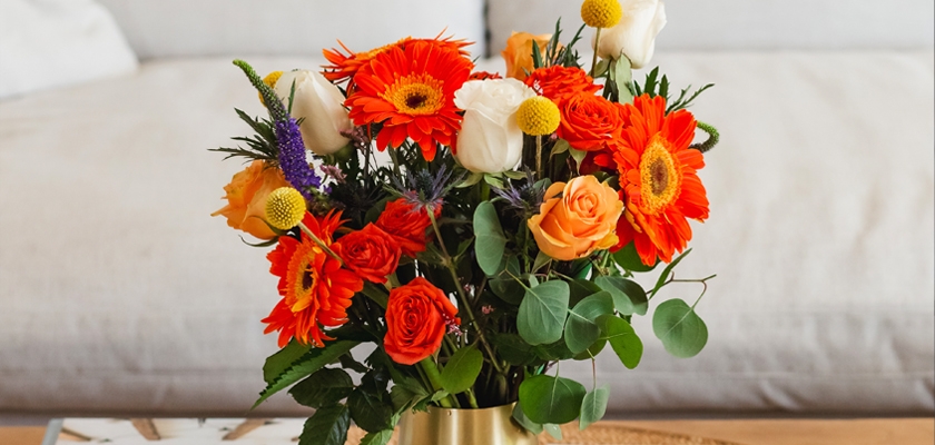 Vibrant floral arrangement featuring orange gerbera daisies, roses, and delicate white blooms.