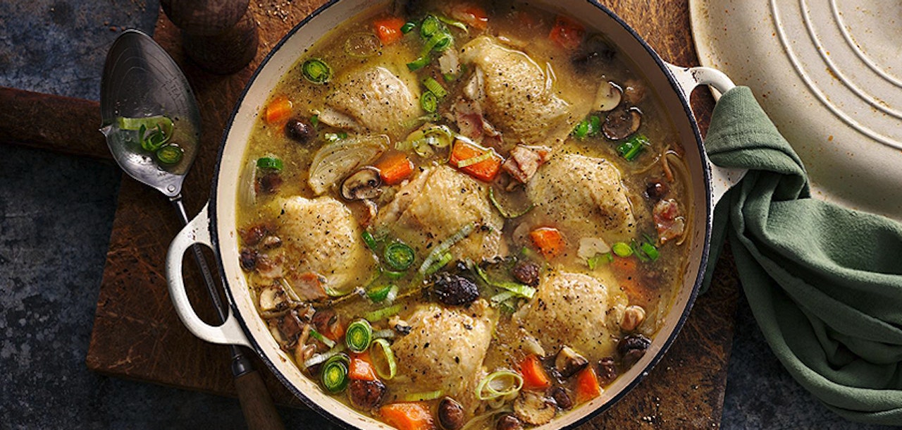 A hearty chicken and dumpling stew with fresh vegetables and herbs in a rustic pot.
