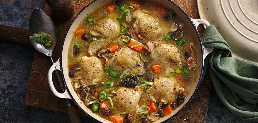 A hearty chicken and dumpling stew with fresh vegetables and herbs in a rustic pot.