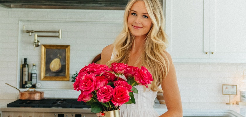 A joyful woman in a kitchen holding a vibrant bouquet of pink roses, adding warmth and beauty.