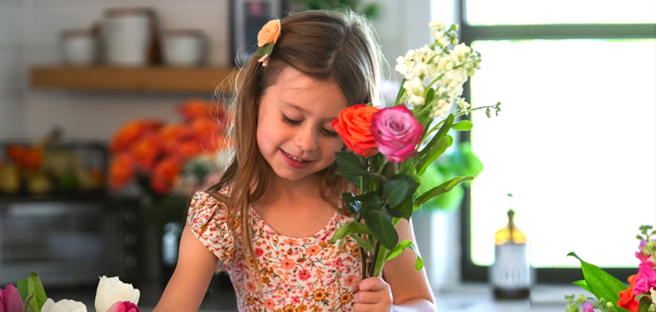 A cheerful girl in a floral dress arranging a vibrant bouquet of colorful flowers at home.