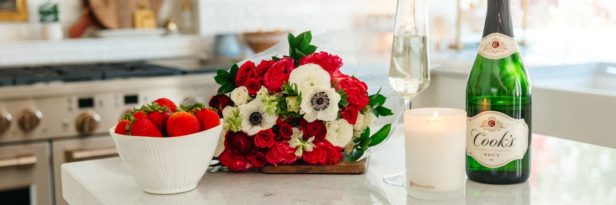 A vibrant floral bouquet with red and white blooms paired with strawberries and champagne.