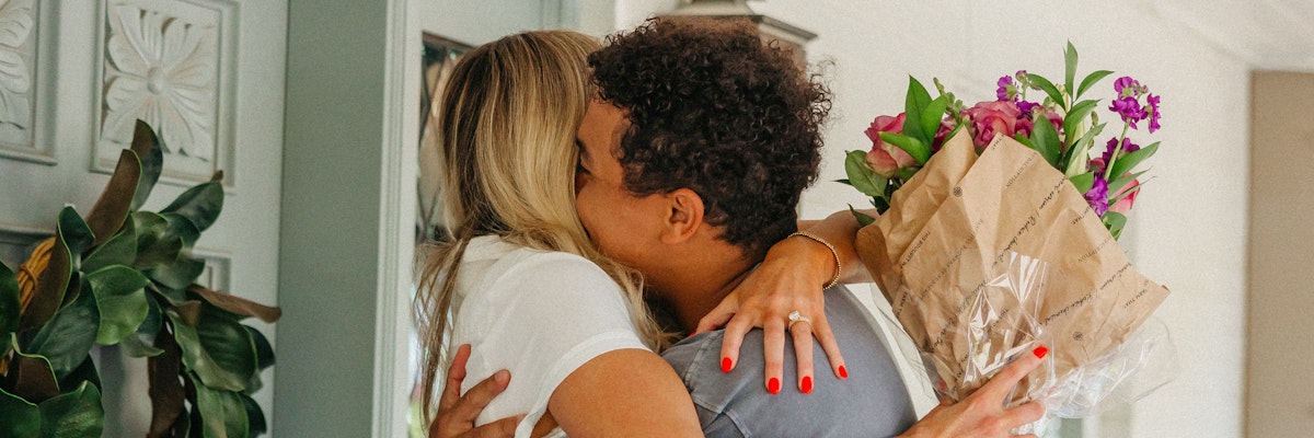 A joyful couple embracing, sharing a moment surrounded by vibrant flowers in a gift bouquet.