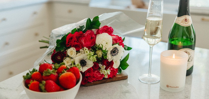 Vibrant floral bouquet alongside champagne, strawberries, and a candle for a romantic celebration.