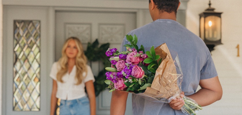 A man surprises a woman at the door with a colorful bouquet, showcasing a joyful greeting moment.